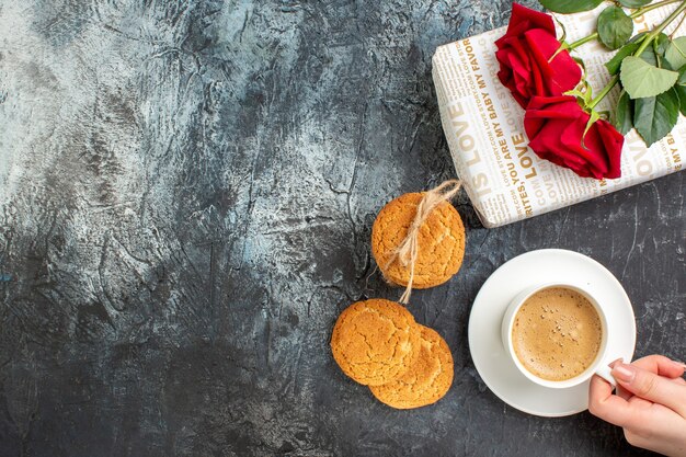 Draufsicht auf rote Rose auf Geschenkbox und Kekse eine Tasse Kaffee auf der linken Seite auf eisigem dunklem Hintergrund