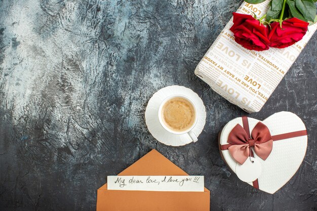 Draufsicht auf rote Rosen und schöne Geschenkboxen mit Brief eine Tasse Kaffee für Geliebte auf eisigem dunklem Hintergrund