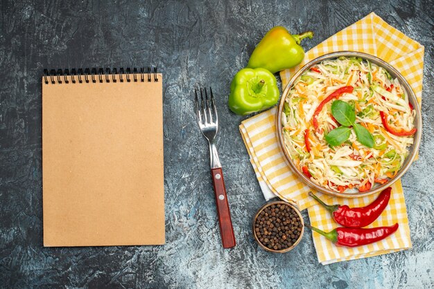 Draufsicht auf Salat mit Zutaten und Notizbuch auf dunkler Oberfläche