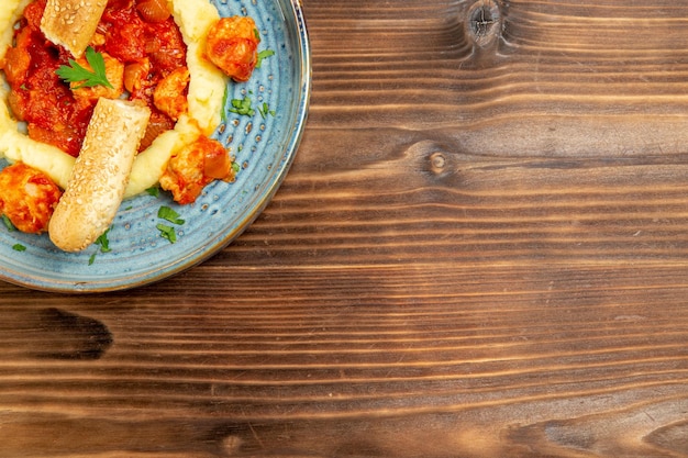 Draufsicht auf Saucenfleisch mit Kartoffelpüree und in Scheiben geschnittenem Brötchen auf braunem Holztisch