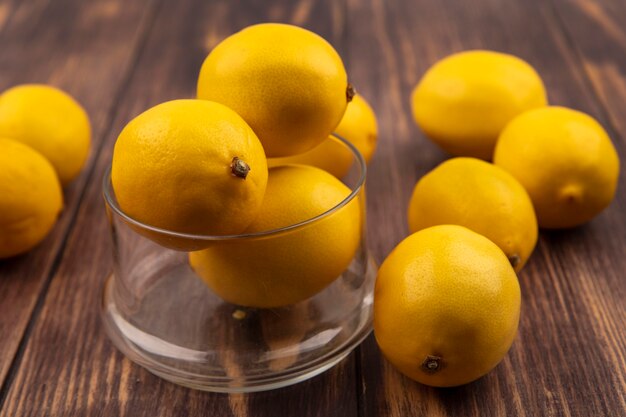 Draufsicht auf sauer schmeckende Zitronen auf einer Glasschale mit Zitronen, die auf einer Holzoberfläche isoliert werden