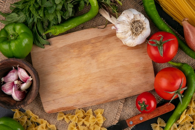 Draufsicht auf Schneidebrett mit Tomaten Knoblauchglocke und Peperoni und Zwiebeln mit Minze auf einer beigen Serviette