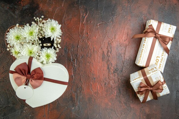 Draufsicht auf schöne Blumen in herzförmiger Schachtel mit Ring und Geschenken auf gemischtem Farbhintergrund mit freiem Platz