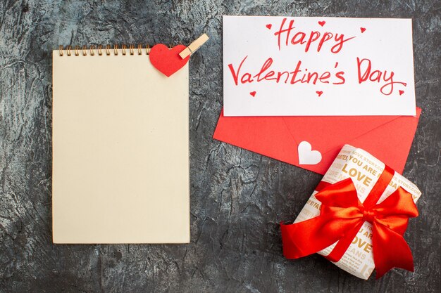 Draufsicht auf schöne Geschenkbox mit rotem Band zum Valentinstag und Notizbuch auf eisigem dunklem Hintergrund