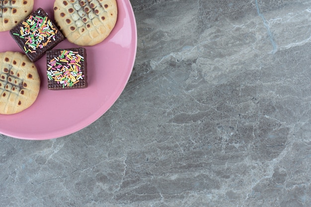 Draufsicht auf Schokoladenwaffel und Kekse auf rosa Teller.