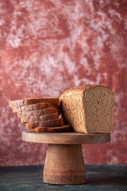 Draufsicht auf Schwarzbrotscheiben auf braunem Holztablett auf gemischtem, beunruhigtem Hintergrund