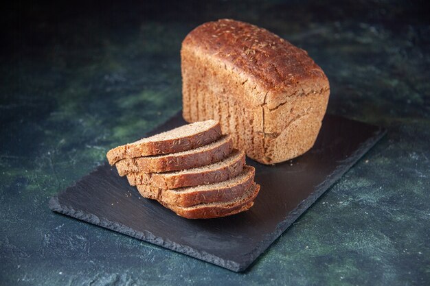 Draufsicht auf Schwarzbrotscheiben auf schwarzem Holztablett auf blauem Hintergrund