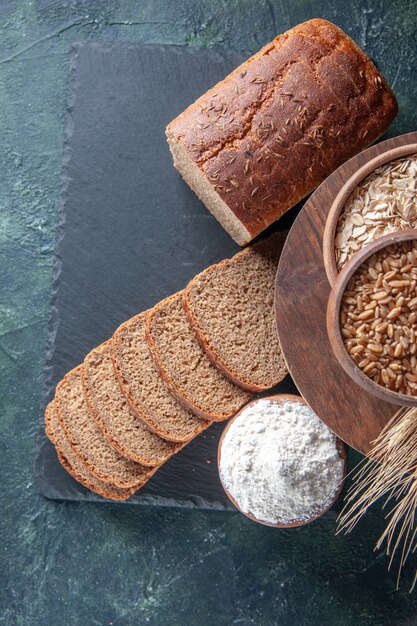 Draufsicht auf Schwarzbrotscheiben auf schwarzem Tablett und Mehl in brauner Schüssel auf dunkelgrünem Hintergrund