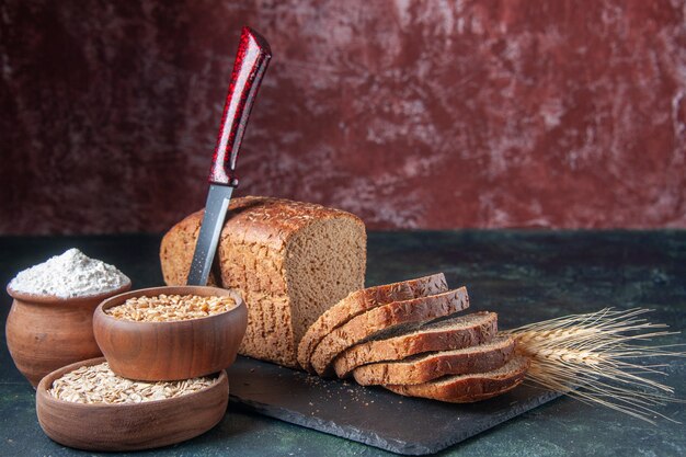 Draufsicht auf Schwarzbrotscheiben Mehl Haferflocken Buchweizen auf dunklem Farbbrett auf gemischtem Farbhintergrund