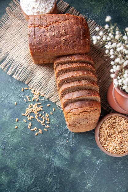 Draufsicht auf Schwarzbrotscheiben Mehl in einer Schüssel und Weizen auf nacktem Farbtuch und Blumentöpfen auf Mischfarbenhintergrund