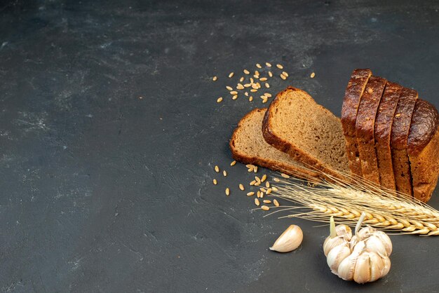 Draufsicht auf Schwarzbrotscheiben Spikes Knoblauch auf der rechten Seite auf schwarzem Hintergrund