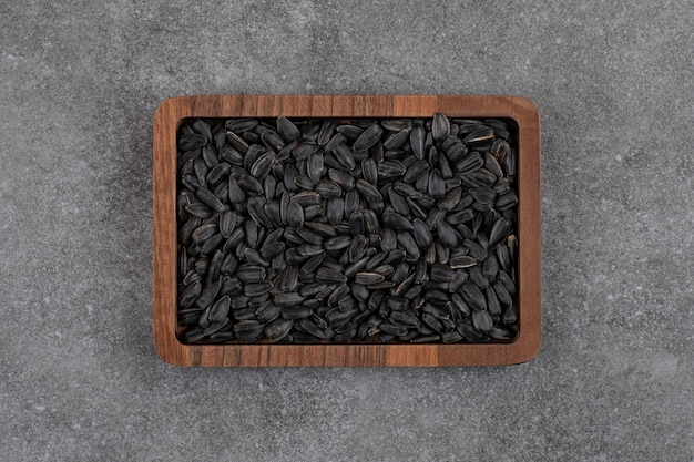 Draufsicht auf schwarze Sonnenblumenkerne auf Holzplatte über grauer Oberfläche