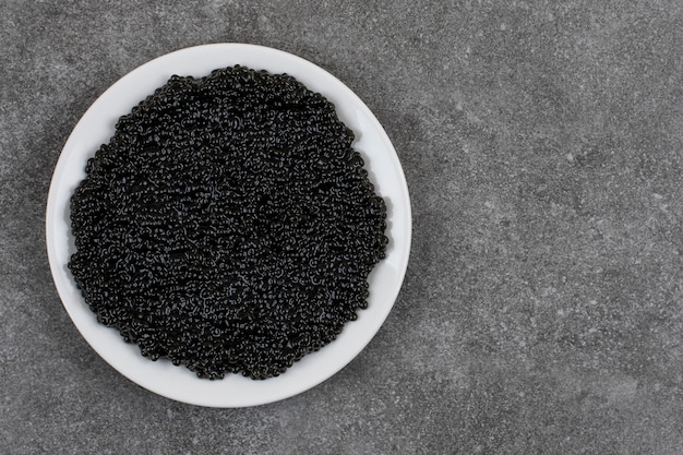Draufsicht auf schwarzen Kaviar auf weißem Teller über grauer Oberfläche