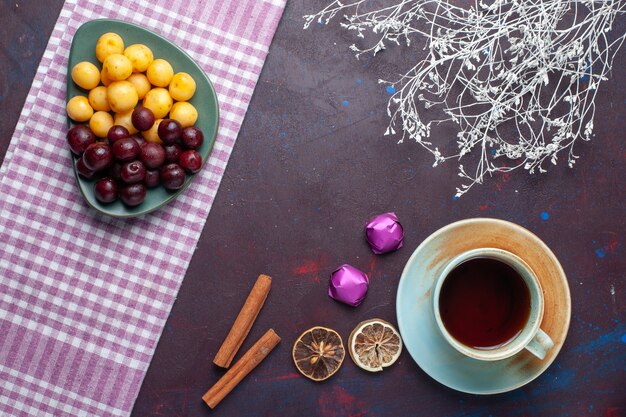 Draufsicht auf Süßkirschen zusammen mit Zimt und Tasse Tee auf der dunklen Oberfläche