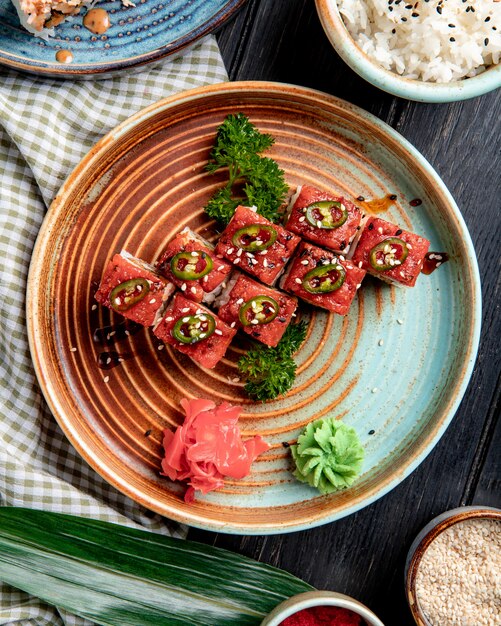 Draufsicht auf Sushi-Rollen mit Thunfisch auf einem Teller mit Ingwer und Wasabi auf Holzoberfläche