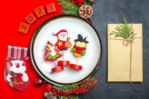 Draufsicht auf Tellerdekorationszubehör Tannenzweige und Zahlenweihnachtssocke auf einer roten Serviette neben Geschenk auf einem schwarzen Tisch