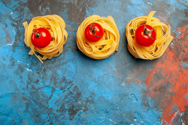 Draufsicht auf tomaten auf hausgemachter pasta, die in einer reihe auf blauem hintergrund aufgereiht sind