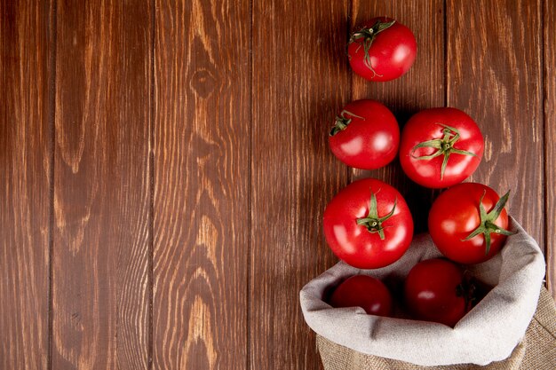 Draufsicht auf Tomaten, die aus dem Sack auf der rechten Seite und der Holzoberfläche mit Kopierraum verschüttet werden