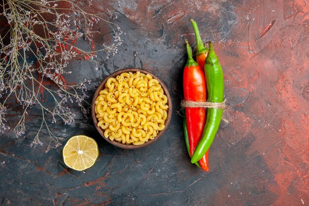 Draufsicht auf ungekochte Pasta-Cayennepfeffer in verschiedenen Farben und Größen, die mit Seil und Zitrone auf gemischtem Farbhintergrund ineinander gebunden sind