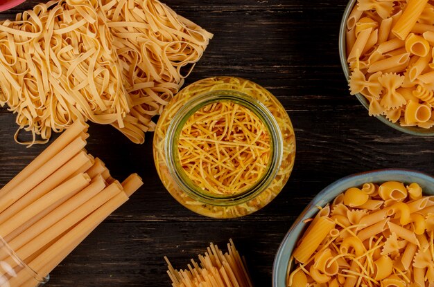Draufsicht auf verschiedene Arten von Nudeln als Bucatini-Spaghetti-Fadennudeln-Tagliatelle und andere auf Holzoberfläche