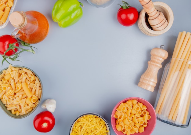 Draufsicht auf verschiedene arten von nudeln als tagliatelle ziti pipe-rigate bucatini mit tomatensalz knoblauch schwarzer pfeffer butter auf blauer oberfläche mit kopierraum