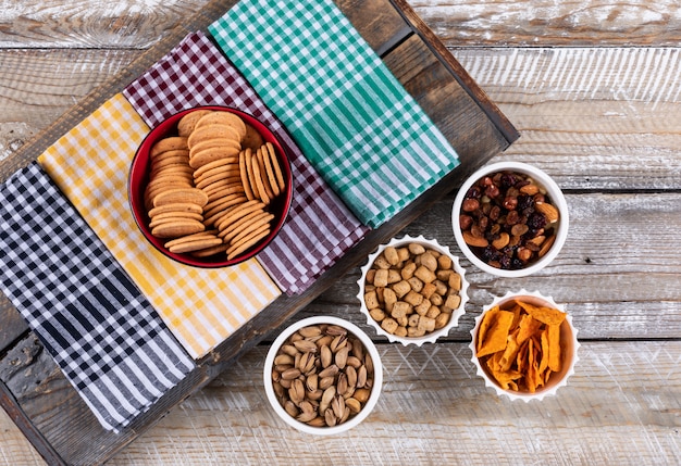 Draufsicht auf verschiedene Arten von Snacks als Nüsse, Cracker und Kekse auf Servietten auf weißer Holzoberfläche horizontal