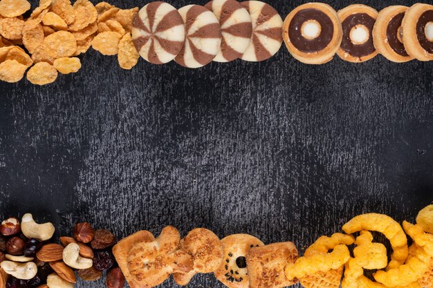 Draufsicht auf verschiedene Arten von Snacks als Nüsse, Cracker und Kekse mit Kopienraum auf dunklem Hintergrund horizontal