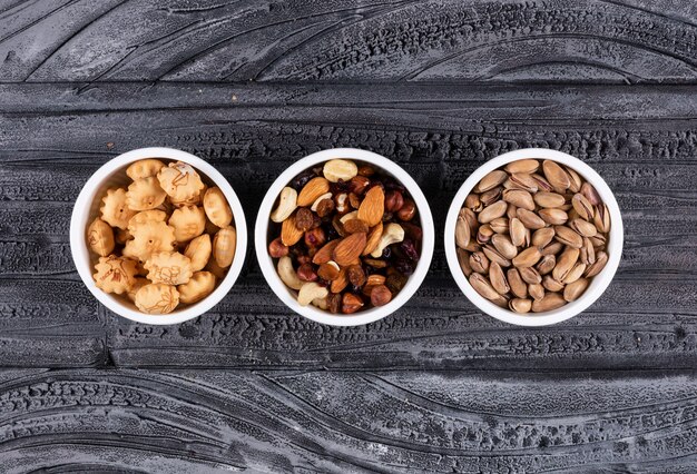 Draufsicht auf verschiedene Arten von Snacks als Nüsse und Cracker in Schalen auf dunkler Horizontaler
