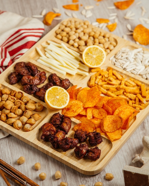 Draufsicht auf verschiedene Biersnacks als gebratene Dushbara gegrillter Hühnerkäse gekochte Kichererbsen und Kartoffelchips auf einem Holzbrett
