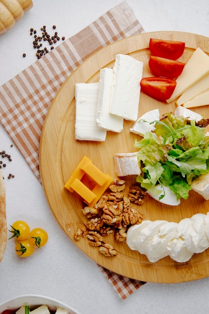 Draufsicht auf verschiedene Käsesorten mit Nüssen auf einem Holzteller