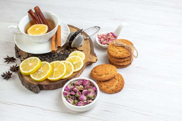 Draufsicht auf verschiedene Kräuter- und Honigschwarztee in einer weißen Tasse und Zitrone auf einem Holztablett Cookies auf weißem Hintergrund