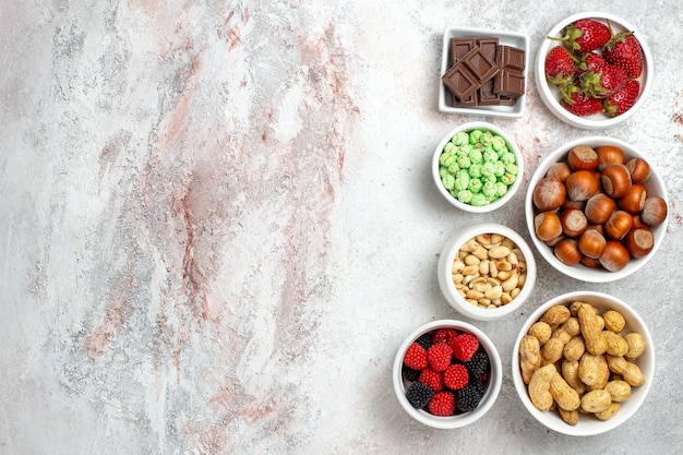 Draufsicht auf verschiedene Snacks Erdnüsse Haselnüsse und Bonbons auf weißer Oberfläche