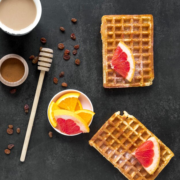 Draufsicht auf Waffeln mit Honigschöpflöffel und Zitrusfrüchten