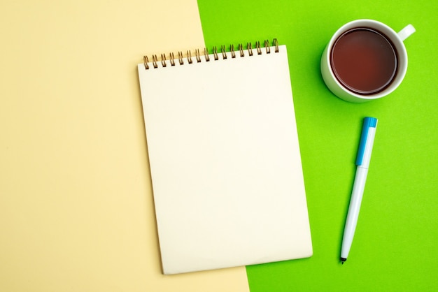 Draufsicht auf weißes Notizbuch mit Stift neben einer Tasse Tee auf weißem und gelbem Hintergrund