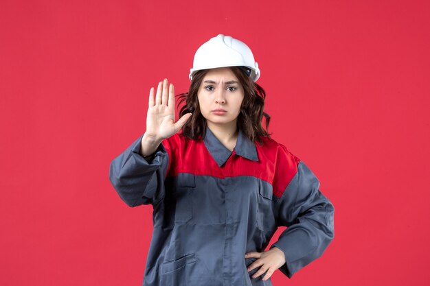 Draufsicht auf wütende Baumeisterin in Uniform mit Schutzhelm und Stoppgeste auf isoliertem rotem Hintergrund