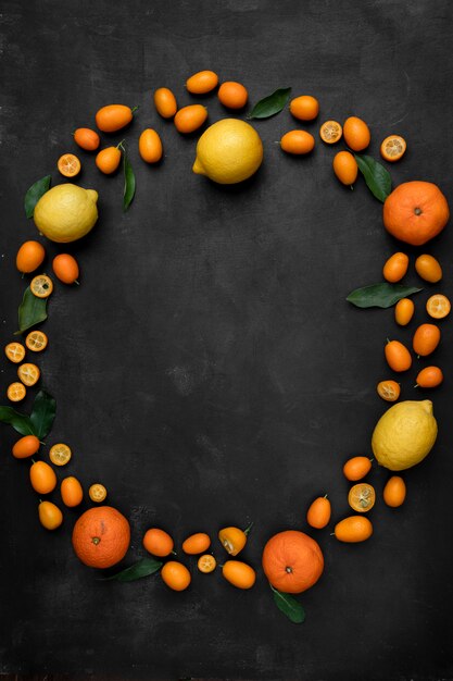 Draufsicht auf Zitrusfrüchte als Kumquats-Zitronen und Mandarinen, kreisförmig auf schwarzer Oberfläche gesetzt