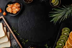 Kostenloses Foto draufsicht auf zitrusfrüchte wie ananas-kiwi-orangen- und mandarinenscheiben kumquat mit brotscheiben in tablett und marmelade in schüssel um untersetzer auf schwarzem hintergrund