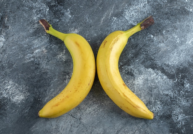 Draufsicht auf zwei frische reife Bananen über grauem Hintergrund.