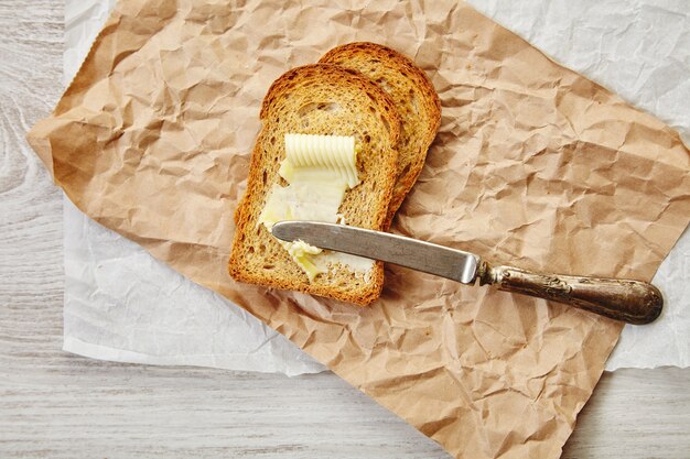 Draufsicht auf zwei Scheiben Roggenbrot als Toast mit Butter zum Frühstück mit Vintage-Messer darauf. Alles auf Bastelpapier.