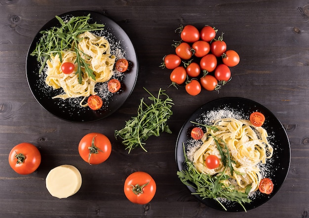 Draufsicht auf zwei schwarze Teller mit Tagliatelle-Nudeln auf Holztisch