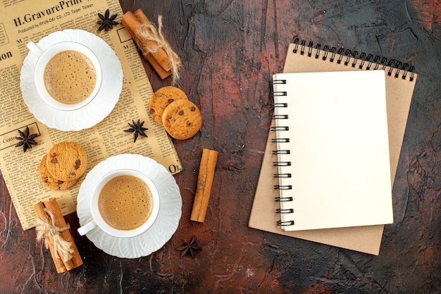 Kostenloses Foto draufsicht auf zwei tassen kaffeeplätzchen-zimt-limonen auf einer alten zeitung und notizbücher auf dunklem hintergrund