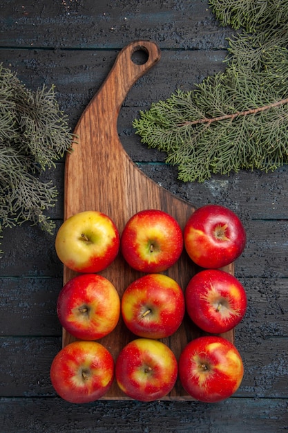 Kostenloses Foto draufsicht aus der ferne äpfel an bord gelb-rötliche äpfel auf einem holzbrett auf grauem tisch zwischen ästen