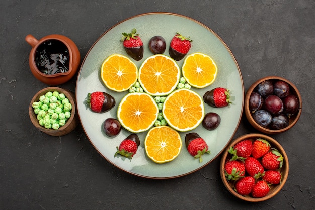 Draufsicht aus der Ferne Beeren und Schokoladenplatte aus gehackten Orangen und mit Schokolade überzogenen Erdbeeren neben den Schalen mit Süßigkeiten Beeren und Schokoladensauce