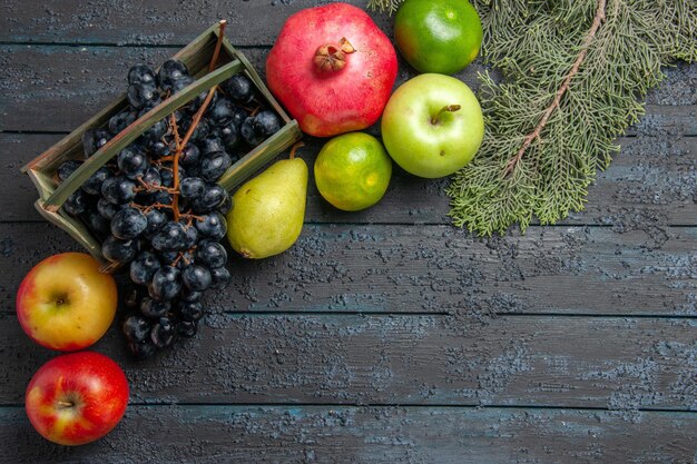 Draufsicht aus der Ferne Früchte auf Tafeltrauben in Holzkiste Granatapfel Birnen Äpfel Limetten neben Fichtenzweigen auf dunklem Tisch