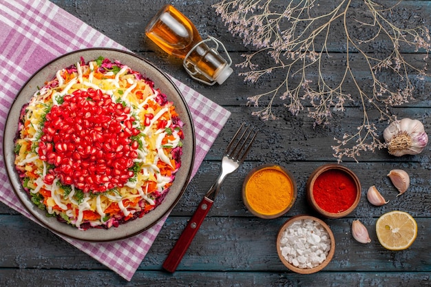 Draufsicht aus der Ferne Granatapfel in der Tellerschale auf der karierten Tischdecke neben den Ästen Gewürze Zitrone Knoblauch Flasche Öl auf dem Tisch