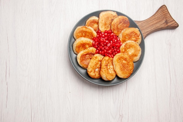 Draufsicht aus der ferne leckerer teller mit appetitlichen pfannkuchen und granatapfel auf dem holzbrett auf dem tisch