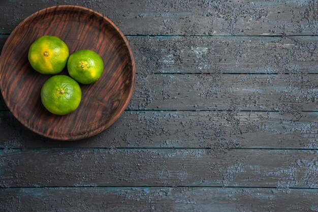 Draufsicht aus der Ferne Limetten auf Teller mit drei Limetten auf der linken Seite des dunklen Tisches