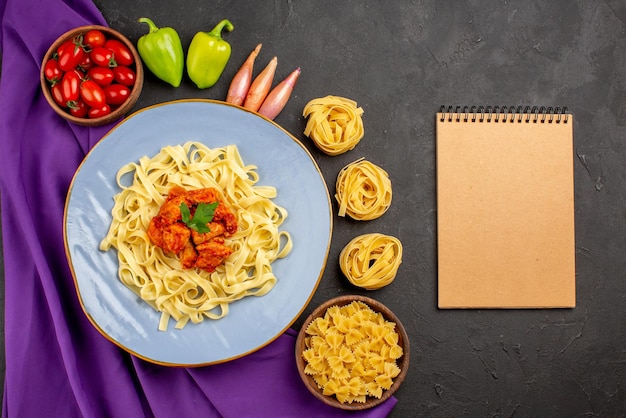 Draufsicht aus der Ferne Pasta und Fleischschüssel mit Tomaten Kugel Pfeffer Zwiebel neben der Creme Notebook Pasta und Teller Pasta auf der lila Tischdecke