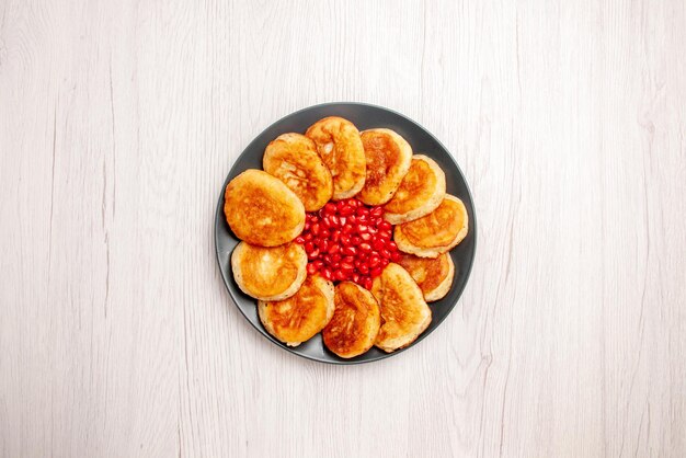 Draufsicht aus der Ferne Pfannkuchen Pfannkuchen und Granatapfel auf dem schwarzen Teller auf dem weißen Tisch