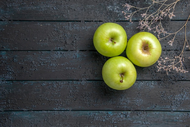 Draufsicht aus der Ferne Äpfel auf Tisch drei appetitlich grüner Apfel neben Ästen rechts vom dunklen Tisch